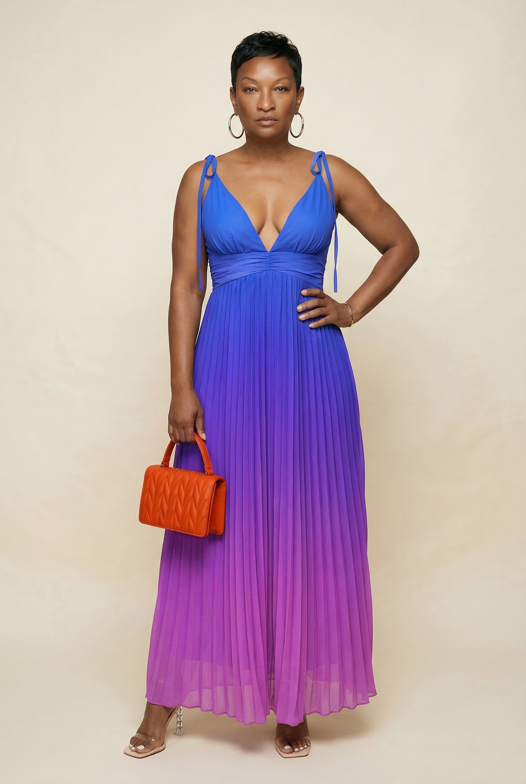 Woman wearing a blue and purple gradient dress holding an orange handbag against a beige background