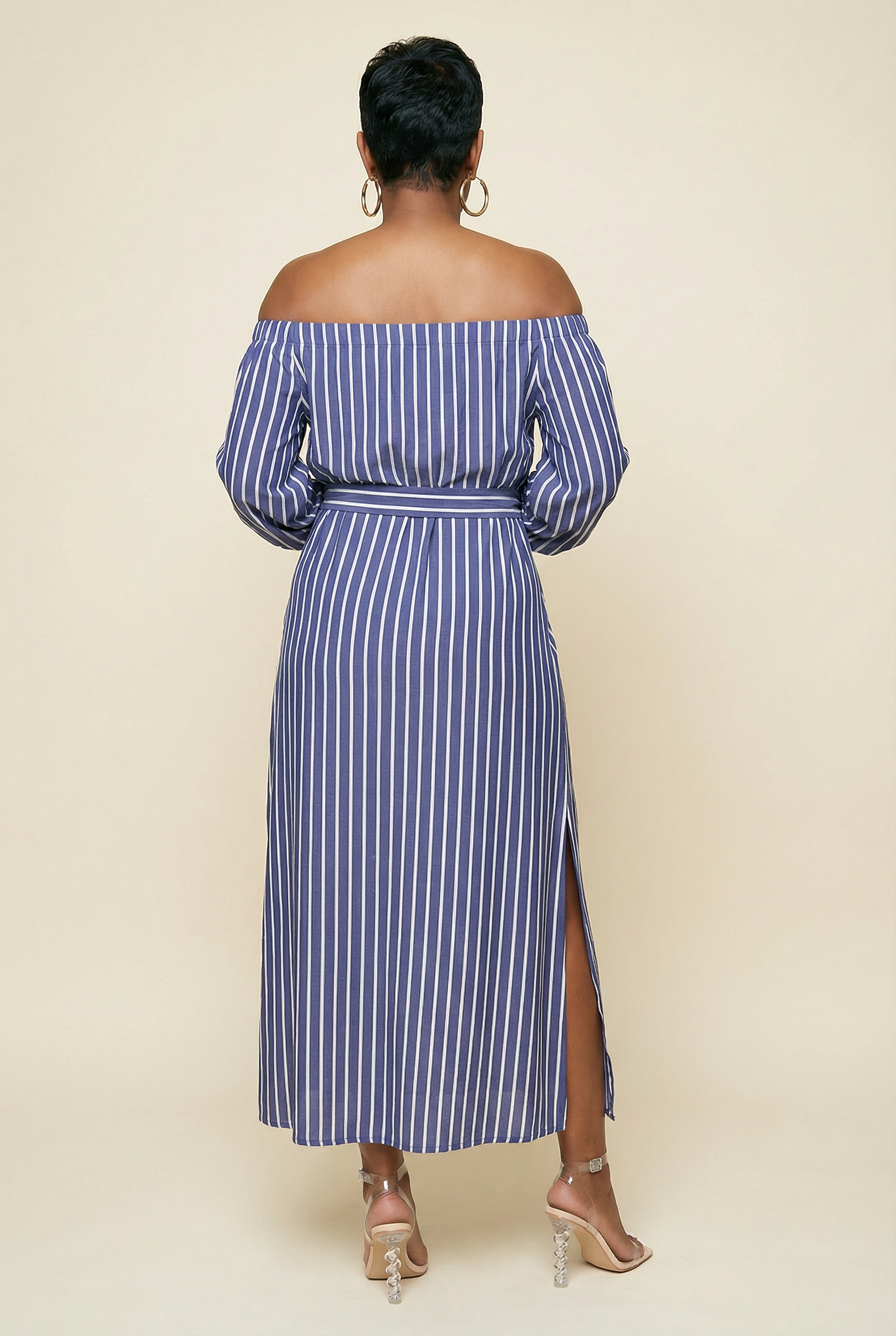 Woman wearing a blue and white striped off-shoulder dress with a slit on a beige background